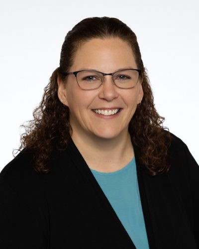 Portrait photo of Kristin wearing a black blazer and glasses, smiling.